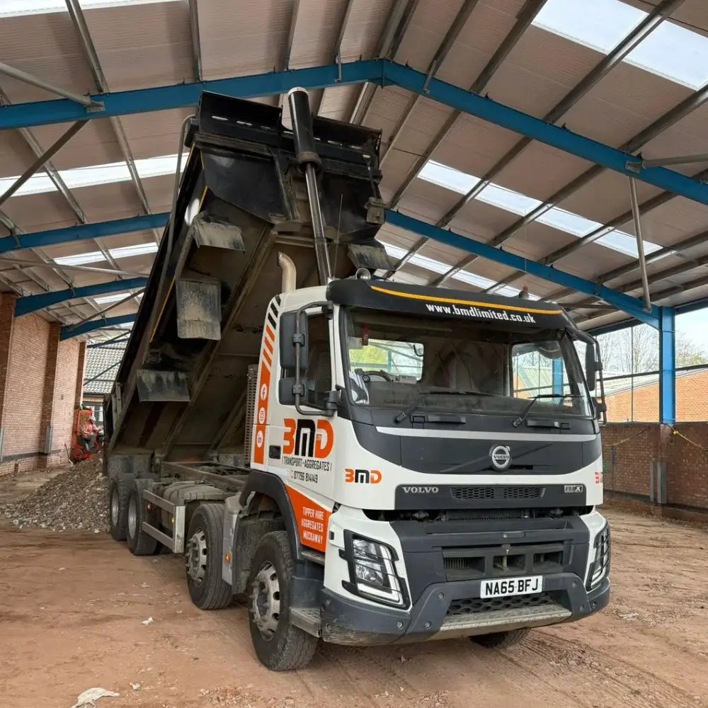 Volvo tipper lorry unloading aggregate materials inside covered yard at Norfolk haulage depot