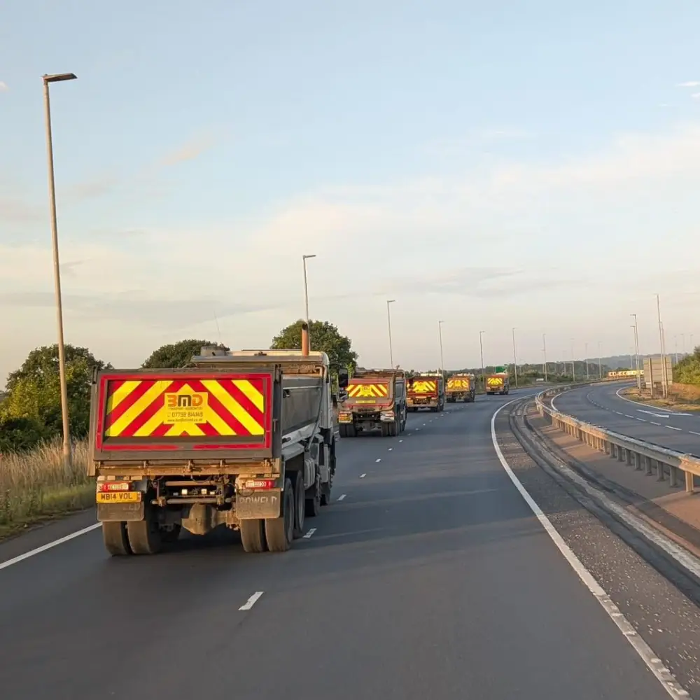 Fleet of tipper lorries travelling in convoy on motorway for bulk haulage operations