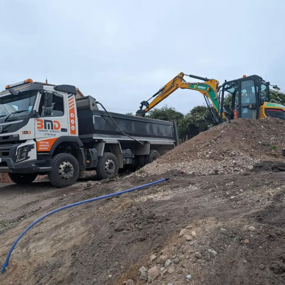 Excavator loading soil into tipper lorry during site clearance and muck away operations